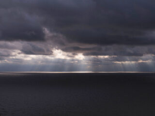 Sun rays shining through dark clouds over water
