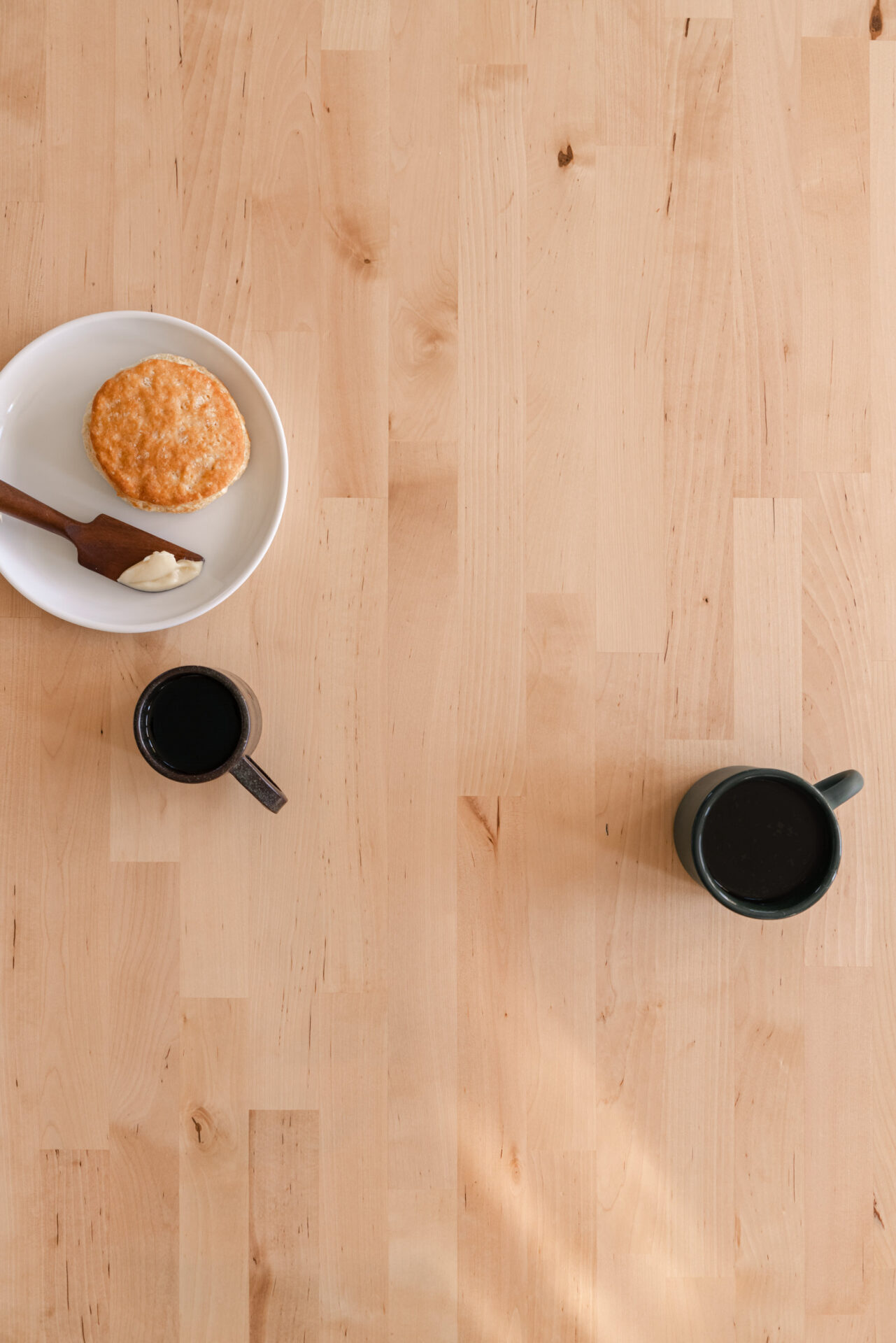 A light wood table with coffee and breakfast on it and light streaming through